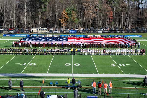 Pre-game national anthem, players and coaches on the field with large American Flag.